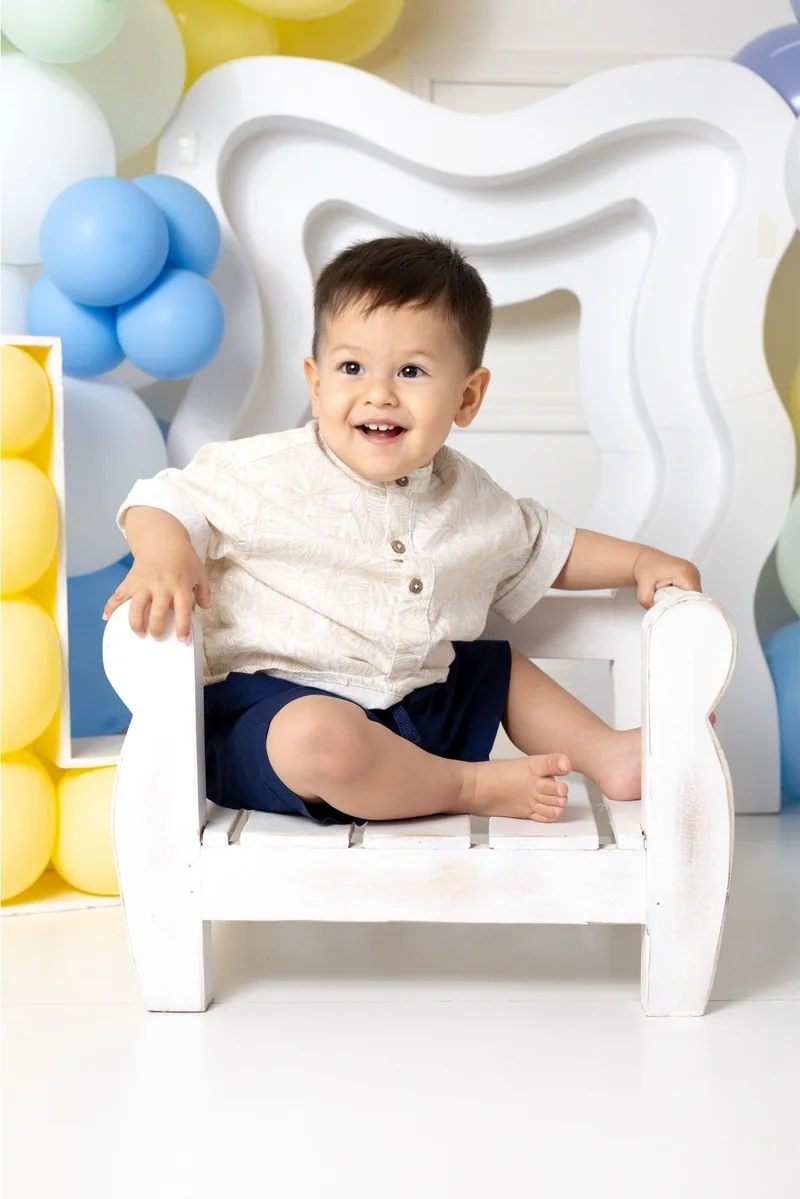 Bebé con camisa clara en una silla blanca del estudio