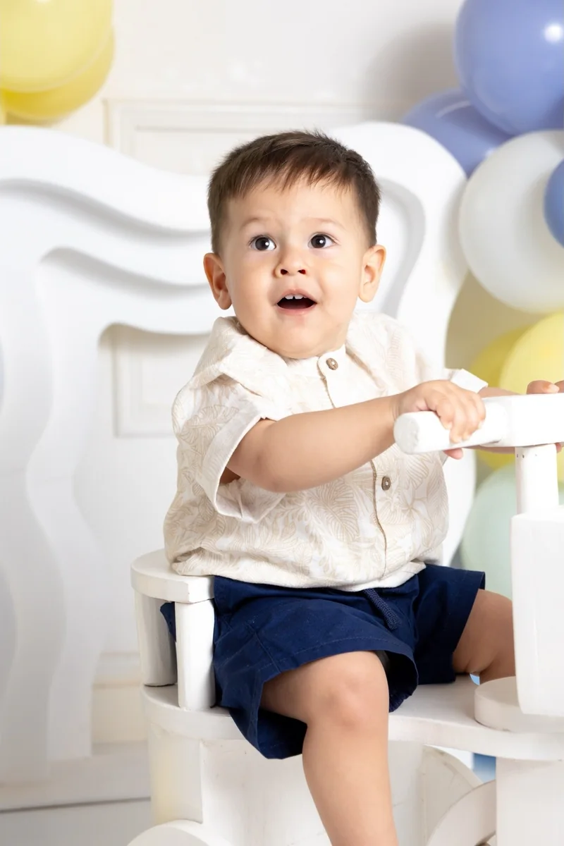 Bebé de un año sentado en un sillón blanco entre globos pastel